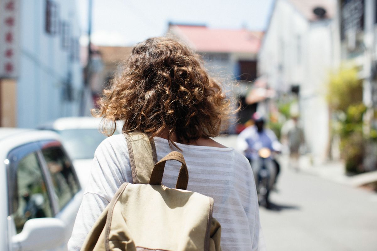 A woman walking away from the camera wearing a backpack with wide padded shoulder straps