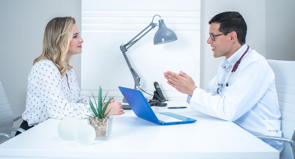 A woman talking with a doctor at a consultation desk in a clinic