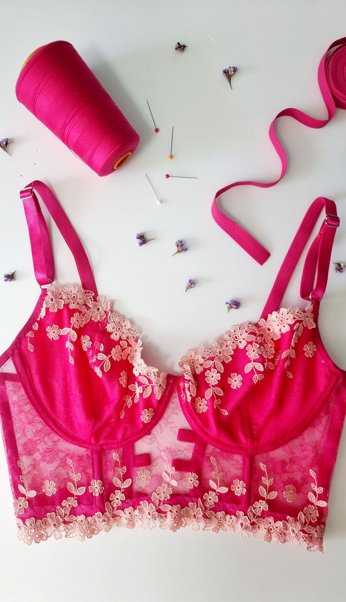 A pink lace longline bra laid flat with thread and pins, showing the extended bra band below the cups