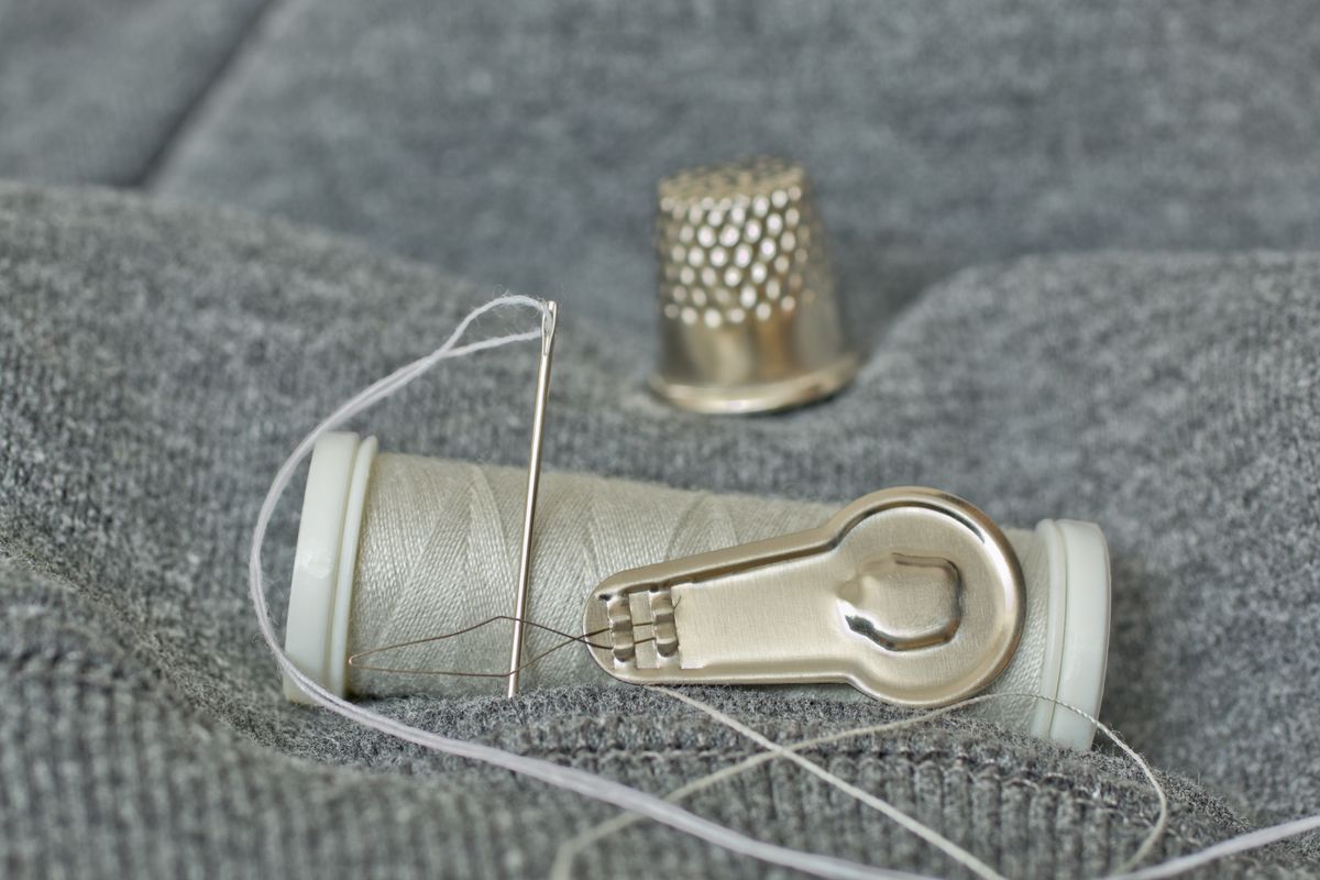 Sewing needle, thread and thimble laid out, a small kit for repairing a poking underwire
