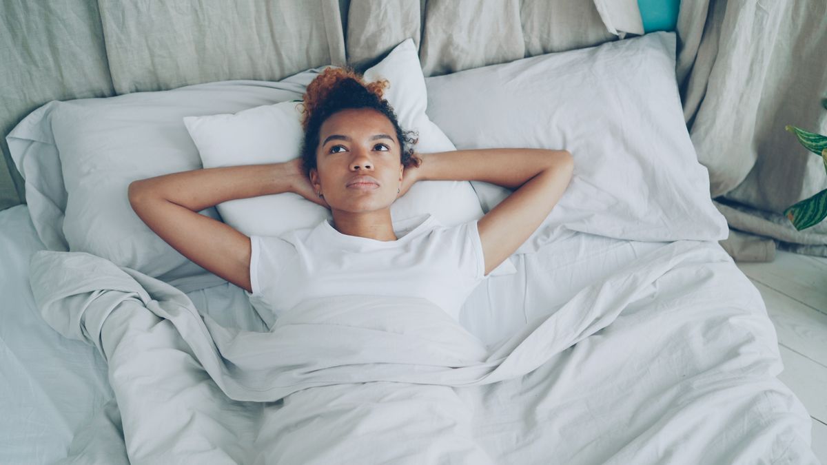 Woman lying in bed in a plain white t-shirt, relaxed, hands behind her head