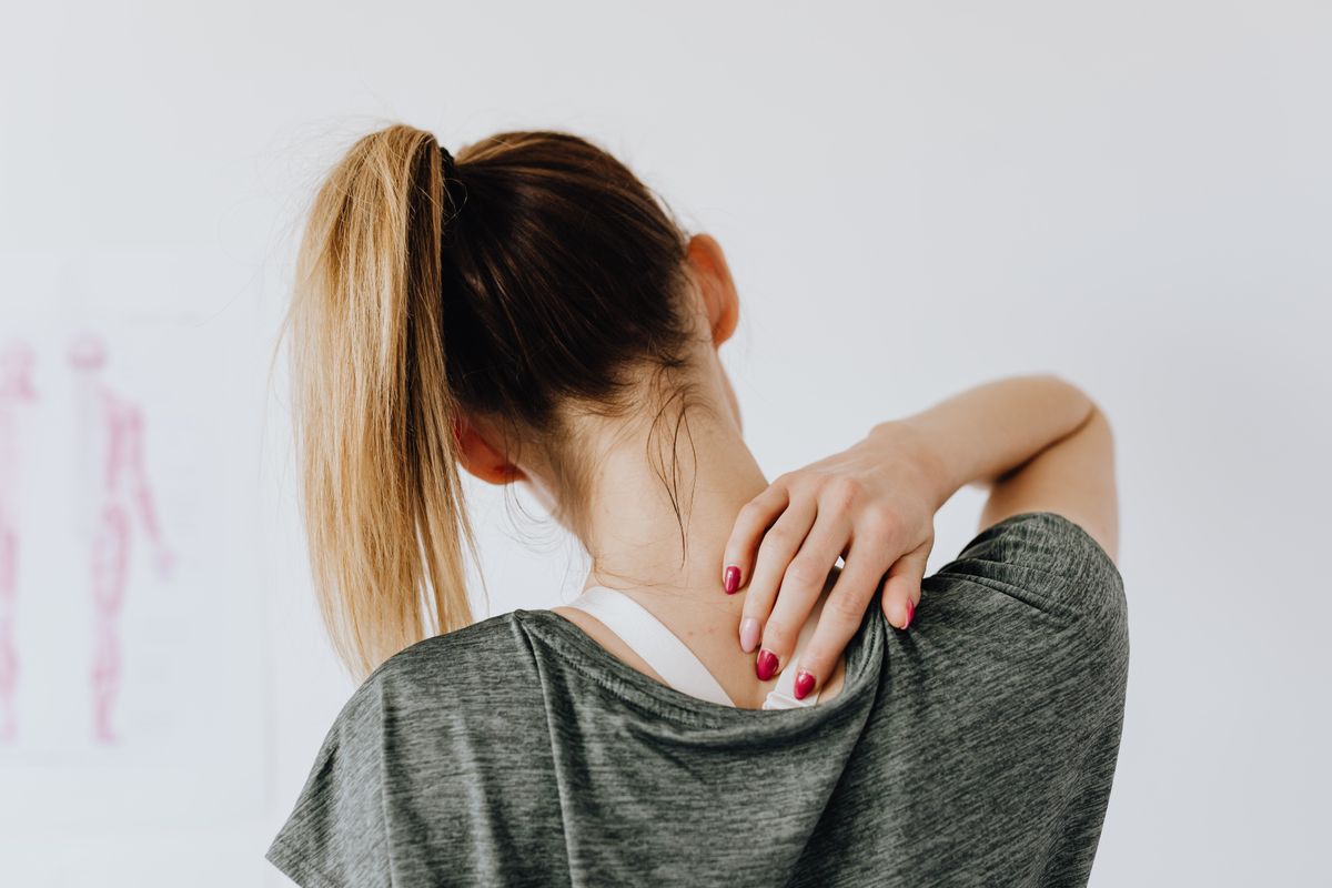 Woman in a tank top holding her shoulder, showing bra straps hurting shoulders pain