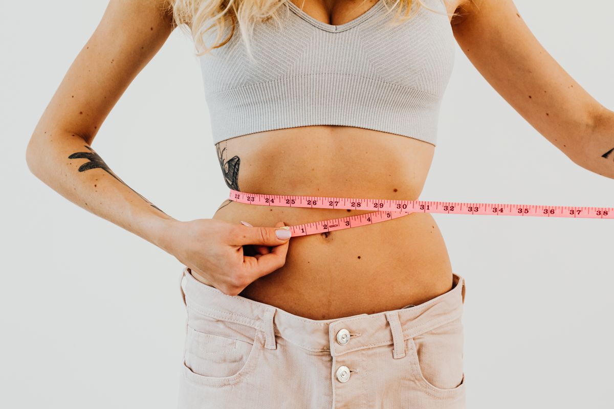 Woman in a sports bra checking her measurement with a tape measure at home