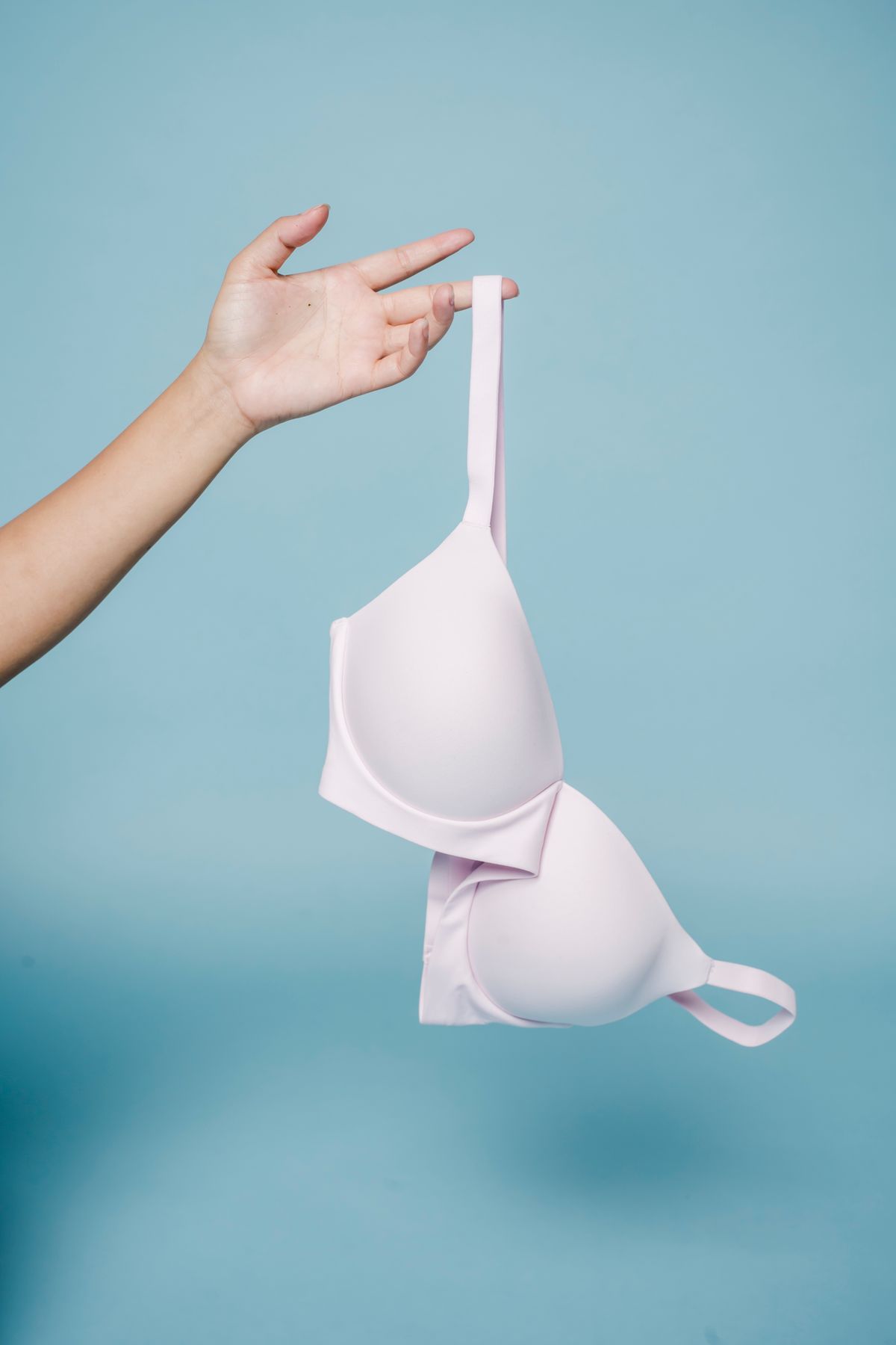 A pale pink moulded bra held up by one strap with the cups empty, showing the gaping shape that means the bra is too big
