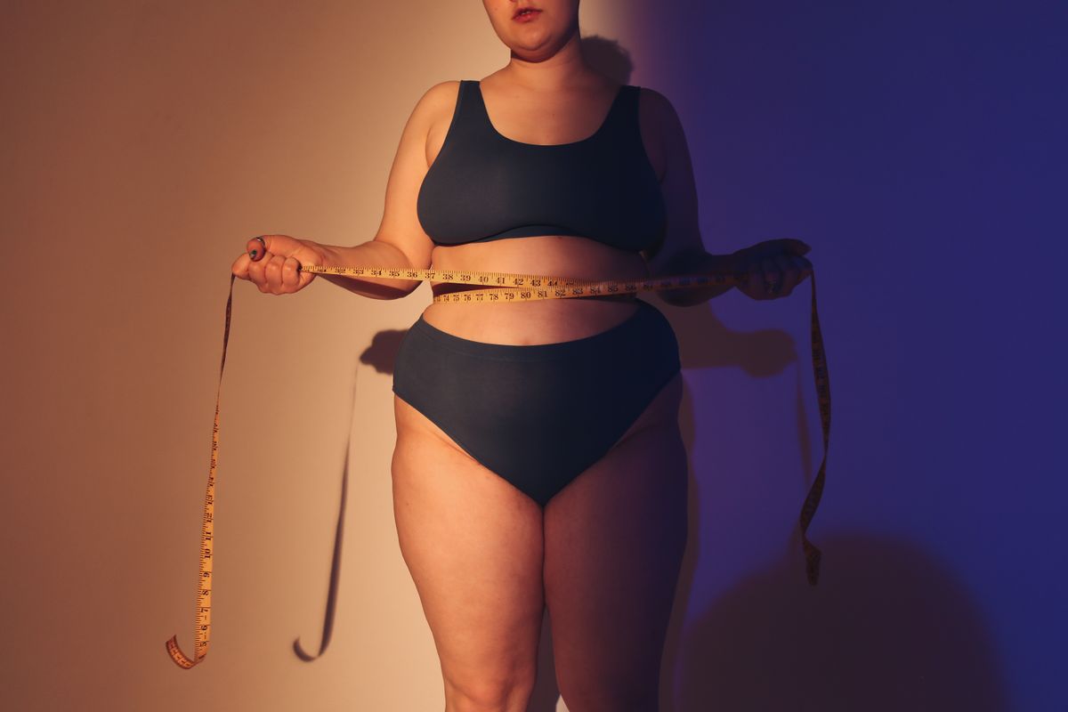 A woman holding a tape measure around her ribcage to find her bra band size