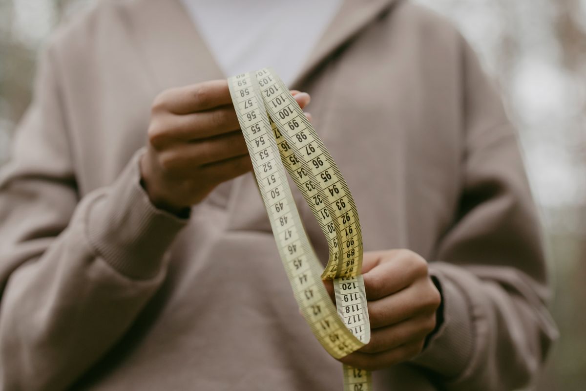 A hand holding a soft measuring tape, used for sister sizing a bra band