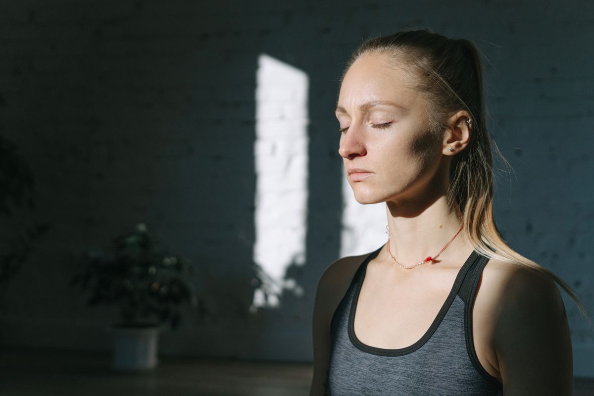 Woman sitting calmly with her eyes closed in a grey vest top, taking a quiet moment