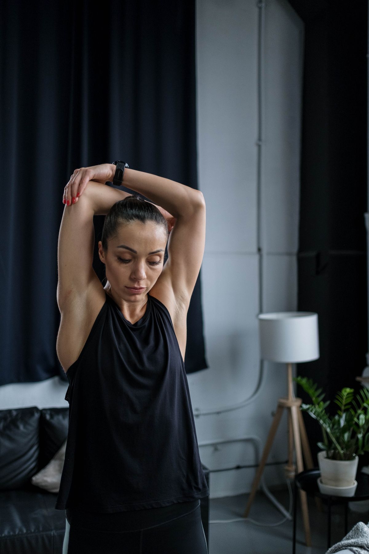 A woman in a black tank top doing a gentle overhead shoulder stretch to relieve bra strap syndrome
