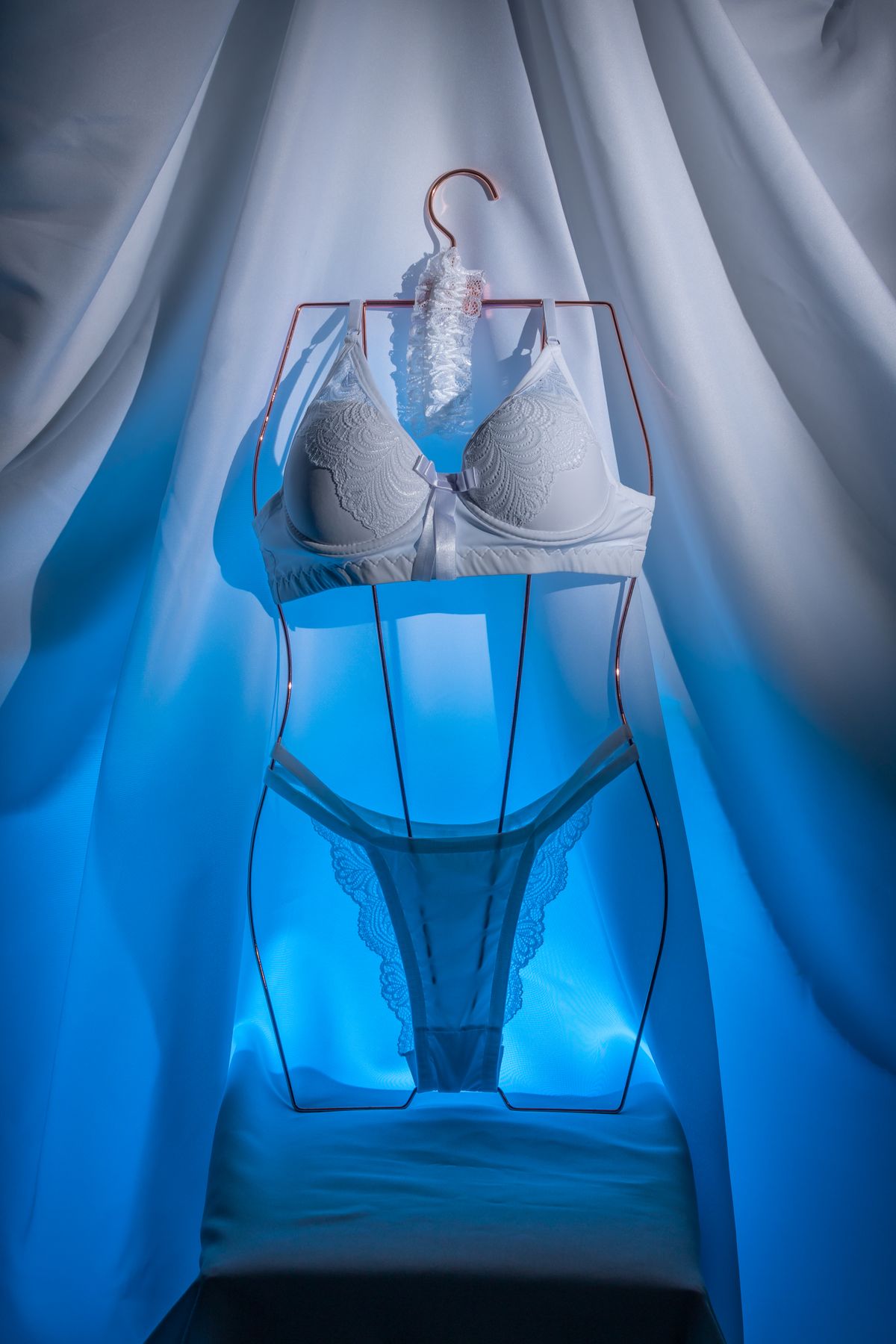A white lace bra displayed on a hanger, showing the band, cups, straps and centre gore